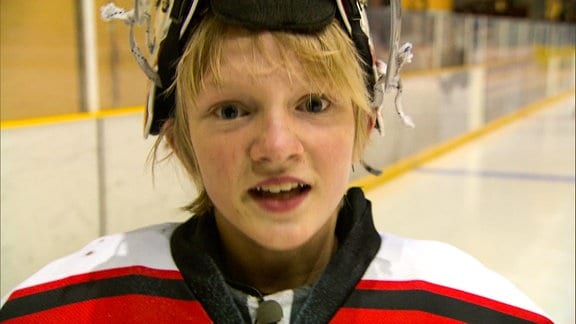 Ein blonder Junge in Eishockeyausrüstung.