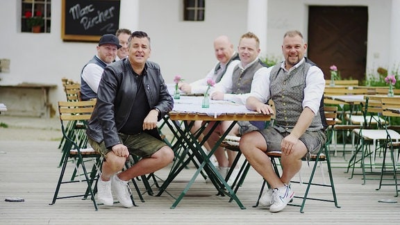 Sechs Männer sitzen in einem Biergarten.