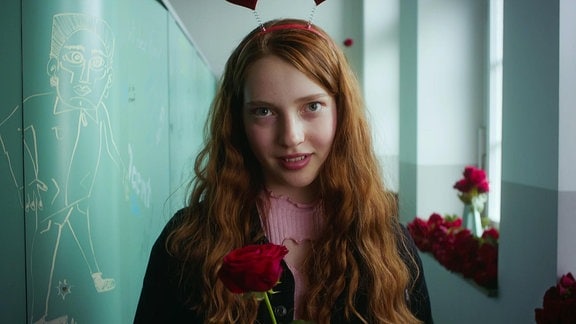 Ein Mädchen mit Rosen und einer Herzchenkrone auf dem Kopf steht auf einem Flur.
