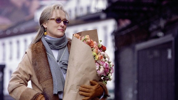 Eine Frau mit Sonnenbrille und einem großen Blumenstrauß im Arm.