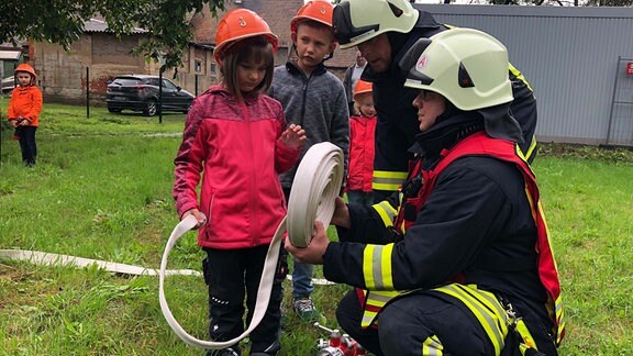 Zwei Kameraden der Freiwilligen Feuerwehr erklären zwei Kindern den Feuerwehreinsatz.