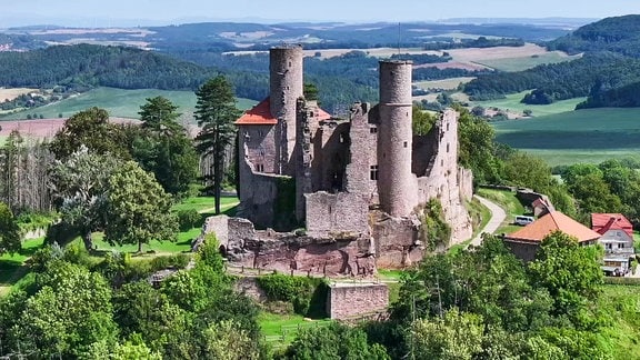 Bick auf eine Burgruine in einer weiten Hügellandschaft.