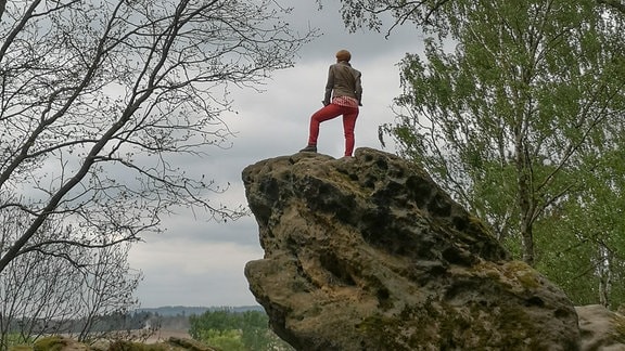 Eine Frau steht auf einem Felsen und schaut in eine weite Landschaft.