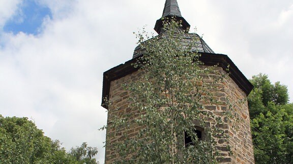Kleiner Turm, umgeben von Bäumen, im Vordergrund eine Frau am Fuße des Turms. 