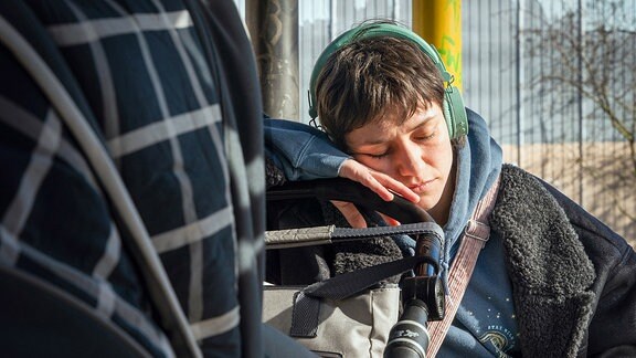 Frau mit Kopfhörern schläft am Kinderwagen ein