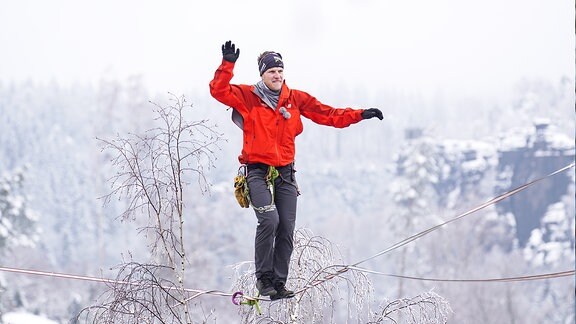 Ein Mann balanciert auf einem Seil zwischen schneebedeckten Bergen. 