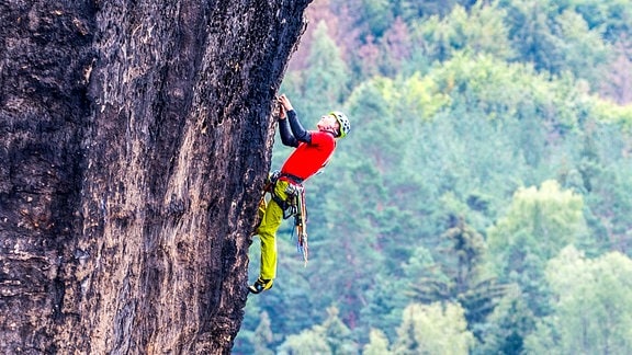 Ein Mann klettert an einer Felswand hoch.