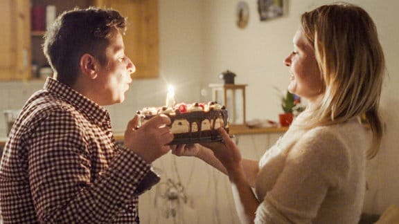 zwei Frauen, eine bläst eine Kerze eines Geburtstagskuchens aus