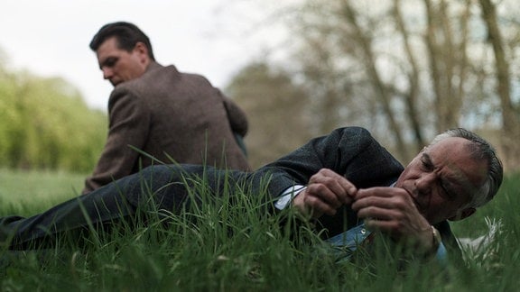 Ein sitzender und ein liegender Mann auf einer Wiese.