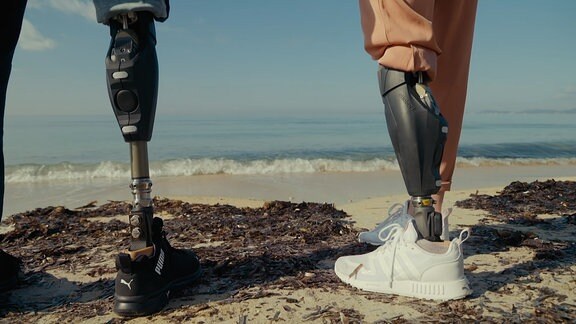 Zwei künstlichen Beinprotesen stehen nebeneinander an einem Strand.