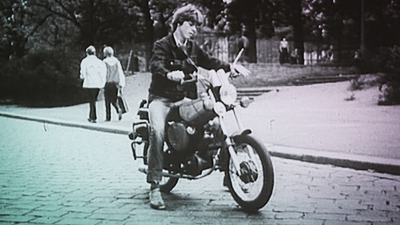 Ein junger Mann mit langen Haaren auf einem Motorrad