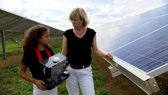 Ein Mädchen steht neben einer Frau auf einem Feld mit Solarpanelen.