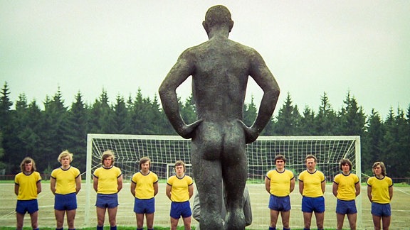 Fußballmannschaft vor Skulptur eines nackten Mannes