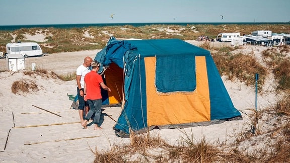 Mann und Frau bauen am Strand ein Zelt auf