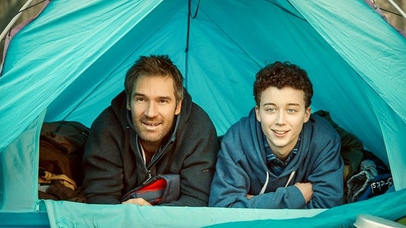 Mann und Junge schauen aus einem Zelt und lächeln