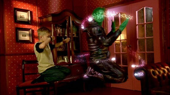 Ein Junge und ein Mann mit grünem Gesicht schweben in einer Art Kampfhaltung über dem Boden eines Zimmers.