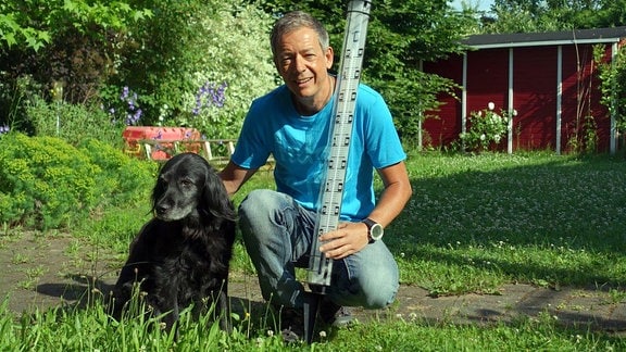 Dr. Ronald Lindner mit einem schwarzem Hund in einem Garten.