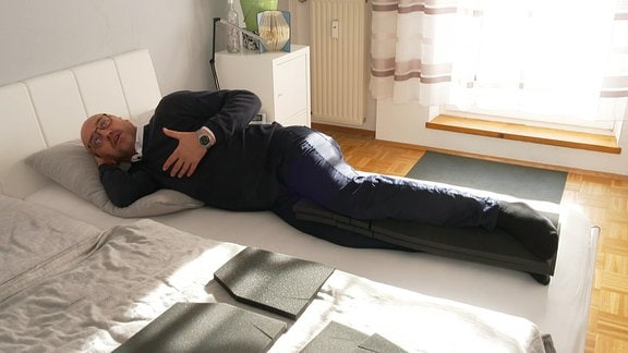 Ein Mann liegt seitlich auf einem Bett mit einer Matte zwischen die Beine geklemmt.