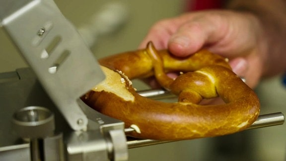 Eine Laugenbrezel wird mit der Hand an eine Maschine gehalten.