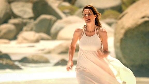 Frau in weißem Kleid rennt an einem Strand