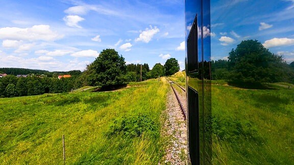 Blick aus einem Zugabteil entlang eines Wagons auf eine grüne Landschaft.