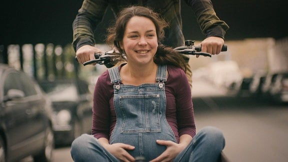 junge, lächelnde, schwangere Frau in einem Fahrrad-Fracht-Wagern