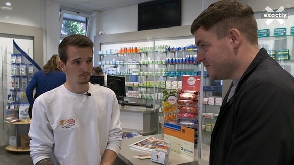 Zwei junge Männer unterhalten sich in einer Apotheke.