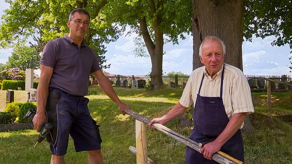 zwei Männer bei Holzarbeiten auf einem Friedhof