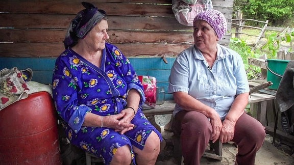 zwei sitzende, ältere Bäuerinnen unterhalten sich in einem Unterstand