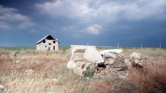Eine unfertiges Einfamilienhaus auf einer Wiese, auf der Betonreste liegen.