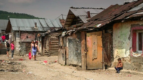 Ein Weg durch halbzerfallene Gebäude auf dem ein paar junge Frauen und ein Junge zu sehen sind.