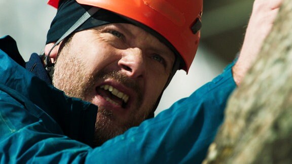 Ein Bergsteiger mit schmerzverzerrtem Gesichtsausdruck