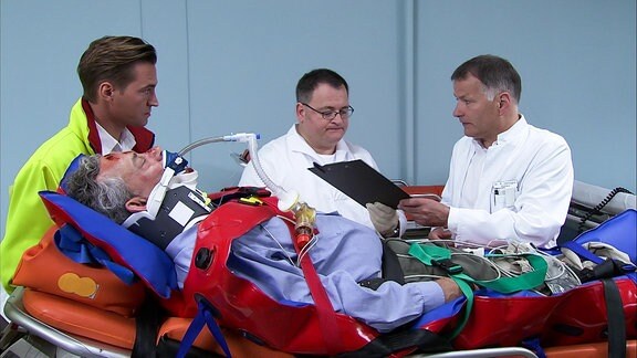 verletzter Patient liegt auf Trage, linke Notarzt, rechts zwei beratende Aerzte