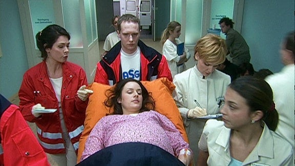 Pfleger und Ärzte um eine Schwangere Frau, die gerade eingeliefert wird.