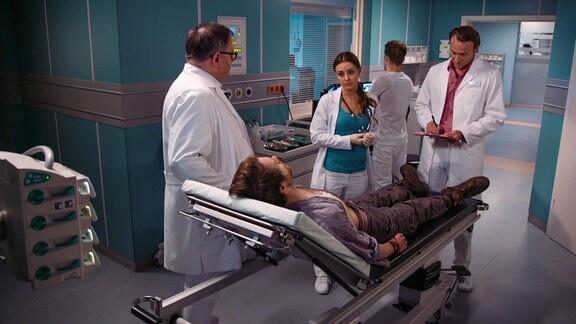 Ärzte stehen um einen Patienten auf einer Liege in einem Behandlungsraum.
