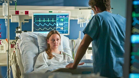 Arzt spricht mit einer im Bett liegender jungen Patientin