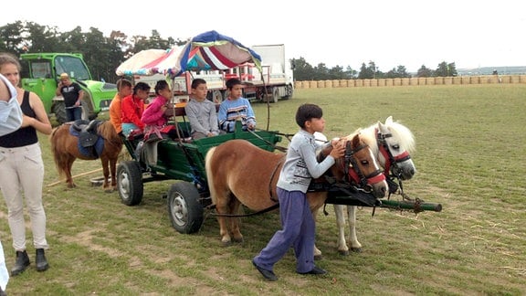 Eine Kutsche mit Kindern, vor die Ponys gespannt sind.