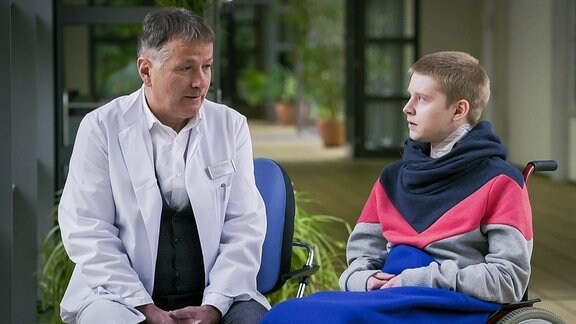 Arzt spricht mit einem im Rollstuhl sitzenden jungen Mann