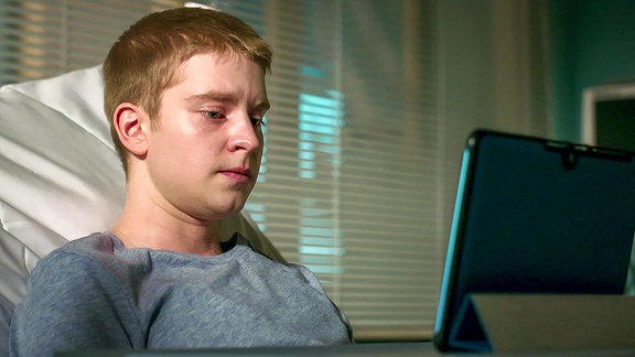 traurig schauender junger Mann sieht in einen Laptop