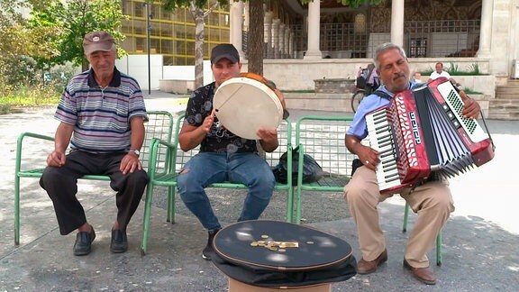 Drei Männer auf einer Bank, zwei musizieren