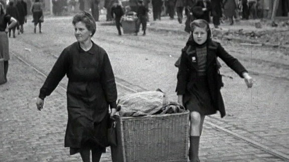 historisches Foto: Frau und Kind tragen einen gefüllten Korb auf einer Straße