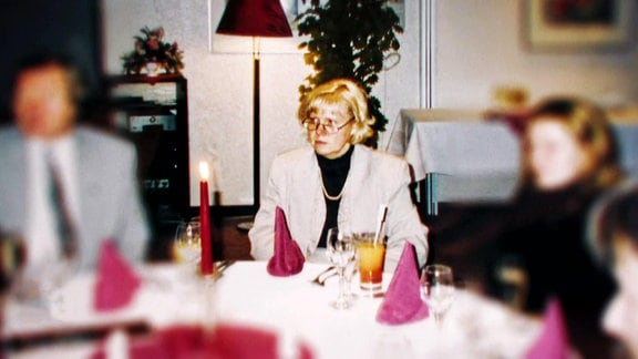 Eine blonde Frau mit Brille an einem feierlich gedeckten Tisch.