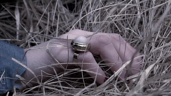 Eine Hand mit einem Ring im Gras.