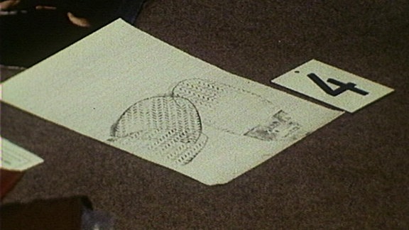 Ein Blatt Papier mit Fußabdrücken und ein Schild mit der Zahl 4 liegen auf einem Teppichboden.