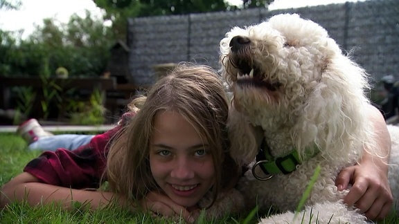 Ein Mädchen liegt mit einem Hund auf einer Wiese.