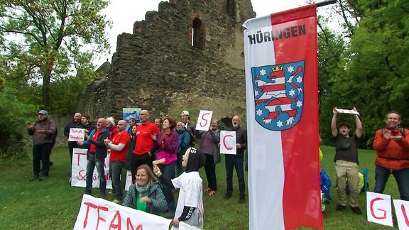 Eine Gruppe Menschen stehen vor einer Kirchenruine und haben eine Thüringenfahne aufgestellt.