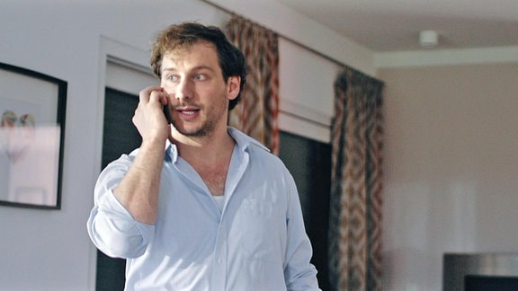 Ein Mann in einer Wohnung telefoniert mit einem Mobiltelefon.