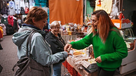Eine Händlerin auf einem Markt legt einer Kundin etwas in die Hand.