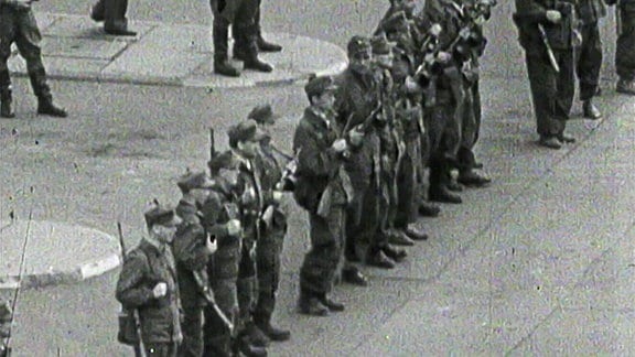 Bewaffnete Männer in Uniform stehen auf einem Platz.
