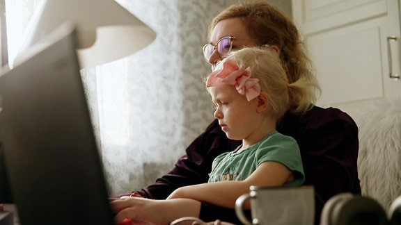 Eine Frau sitzt mit einem Kind auf dem Schoss vor einem Computerbildschirm.